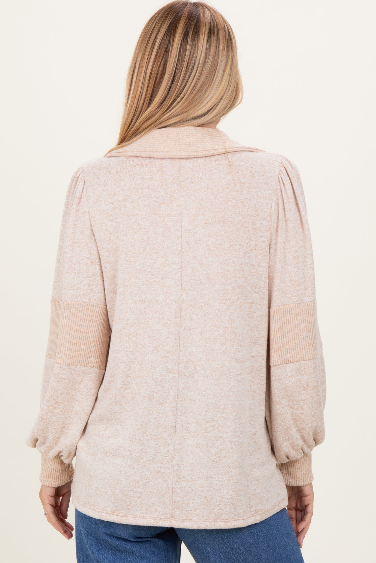 woman wearing a beige oversized sweater with balloon sleeves and ribbed detailing, viewed from the back