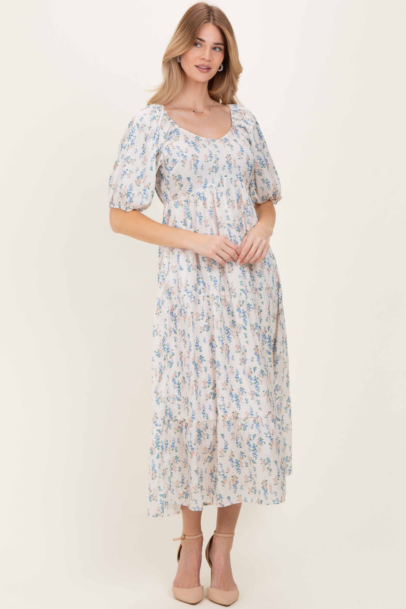 woman wearing a floral-printed maxi dress with puff sleeves and a square neckline, standing in neutral heels