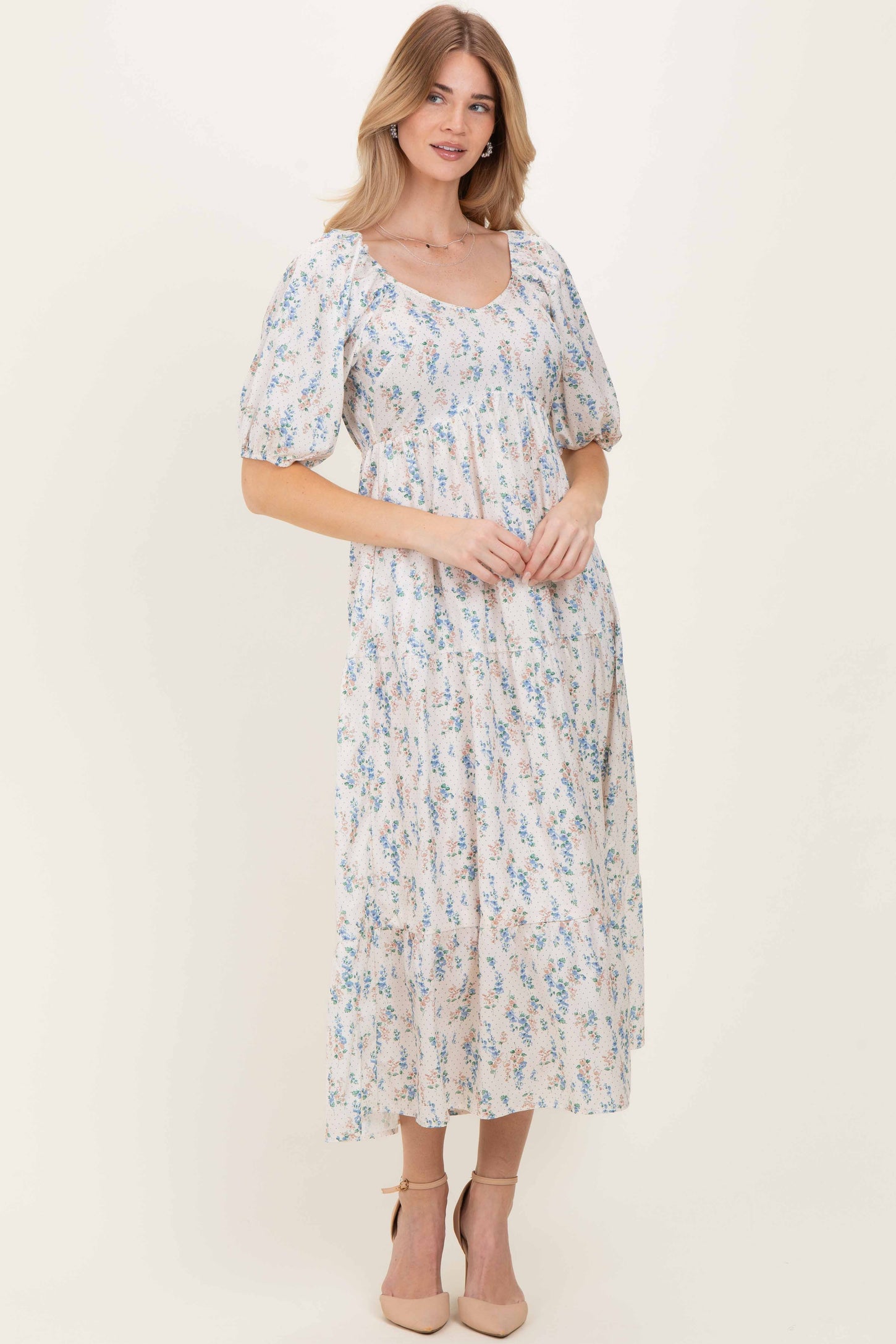 woman wearing a floral-printed maxi dress with puff sleeves and a square neckline, standing in neutral heels