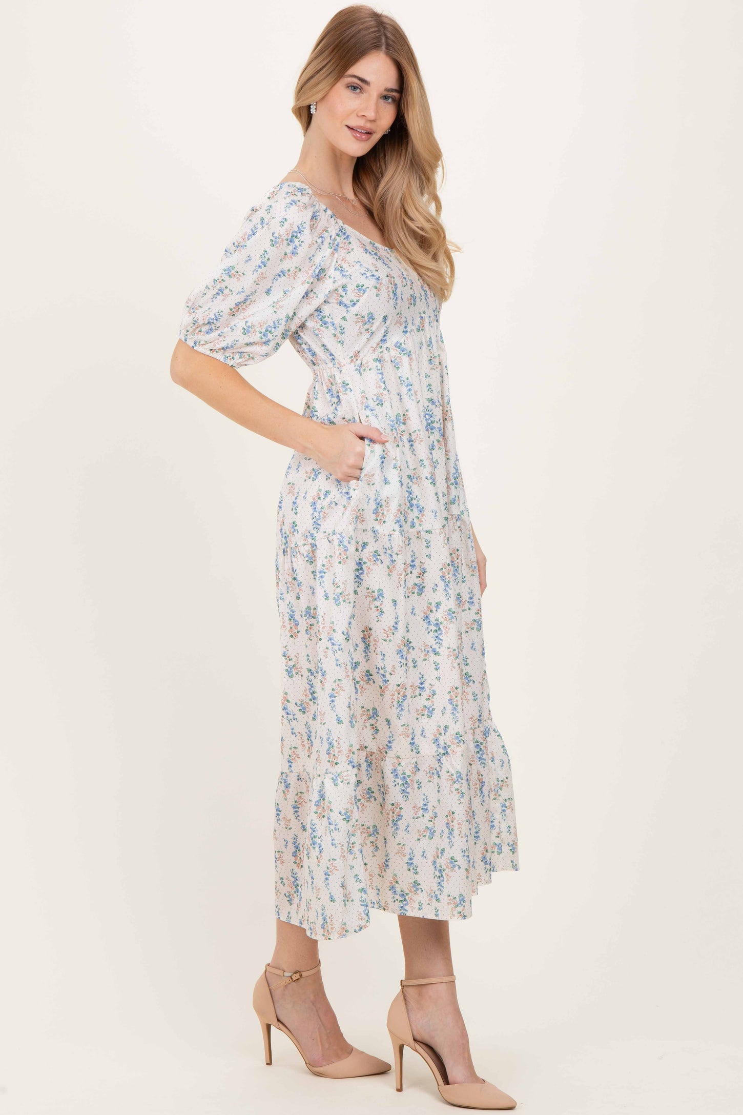 woman wearing a floral midi dress with puff sleeves and pockets in a light pastel color, styled with beige heels