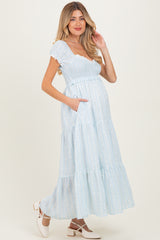 woman wearing a light blue maternity maxi dress with tiered ruffles and pockets, showing a baby bump