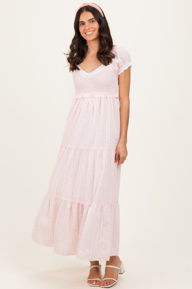 woman wearing a pink floral maxi dress with short puff sleeves and a tiered skirt standing against a neutral background