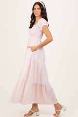 woman wearing a pink tiered maxi dress with a smocked bodice and puff sleeves, standing sideways with hands in pockets