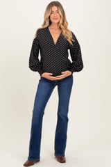 woman wearing a black and white polka dot maternity top and blue flared jeans, holding her baby bump