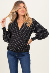 woman wearing a black maternity wrap blouse with white polka dots and puff sleeves, smiling and posing with one hand in her hair