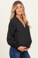 woman wearing a black maternity top with white polka dots and a deep v-neck, cradling her baby bump