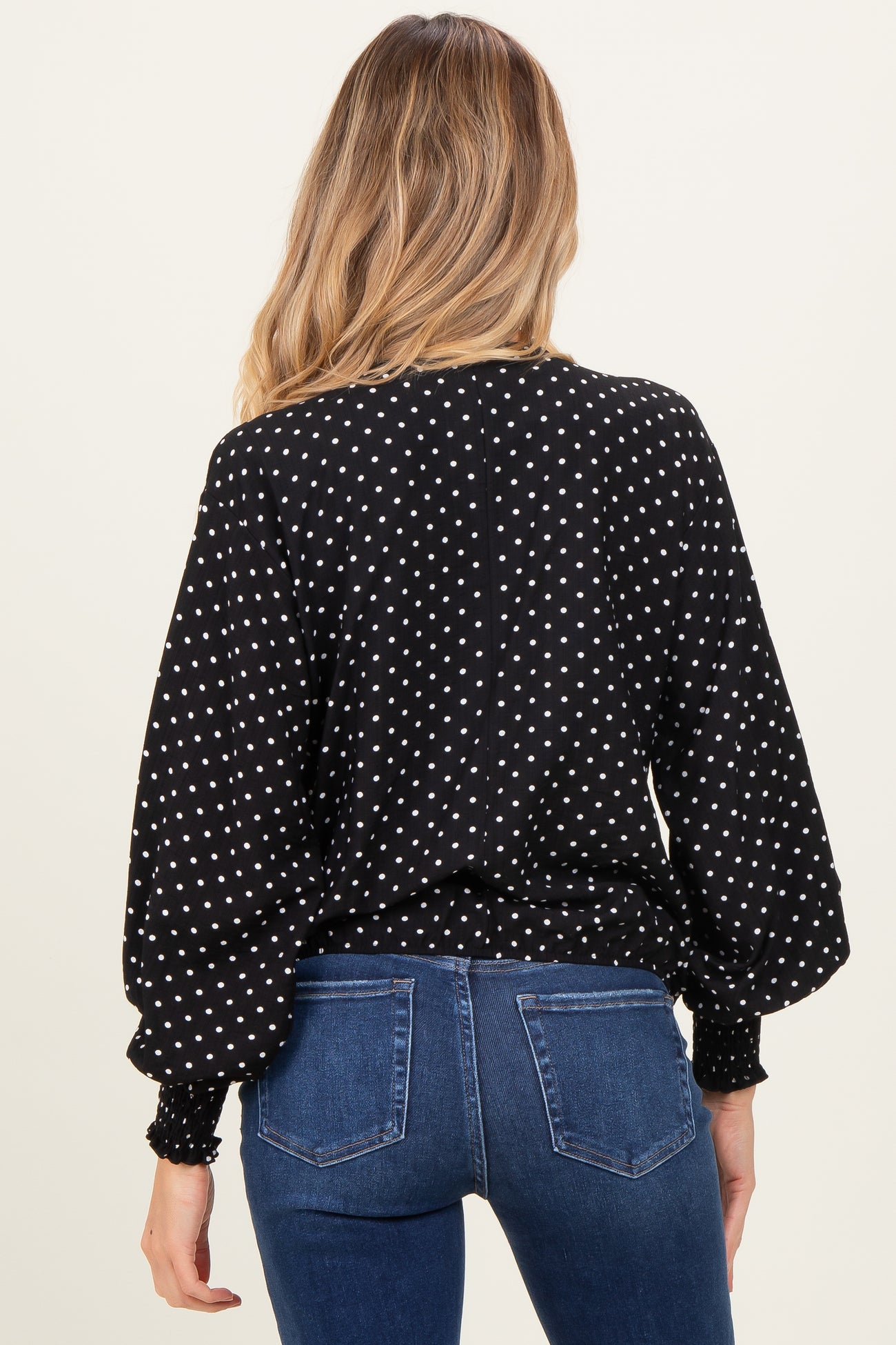 woman wearing a black maternity top with white polka dots and balloon sleeves, view from the back
