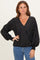 woman wearing a black polka dot wrap blouse with long sleeves and smocked cuffs, styled with blue jeans