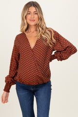 woman wearing a rust-colored maternity wrap top with white polka dots and puffed sleeves, styled with blue jeans