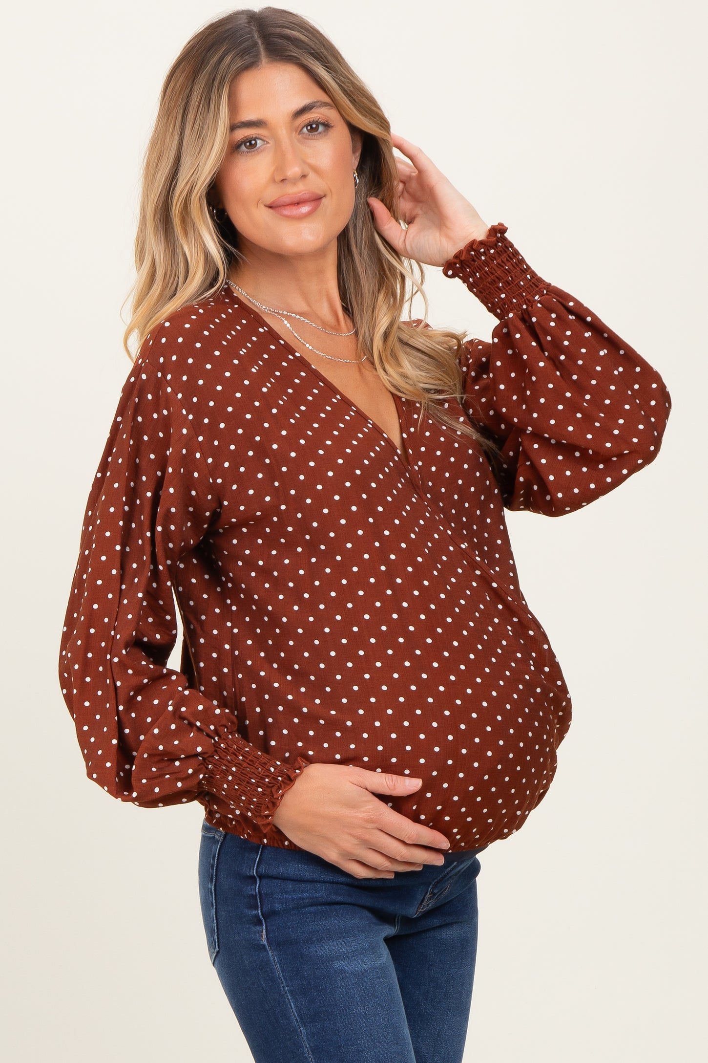 woman wearing a brown polka dot maternity top with a deep v-neckline and puff sleeves, showing her baby bump
