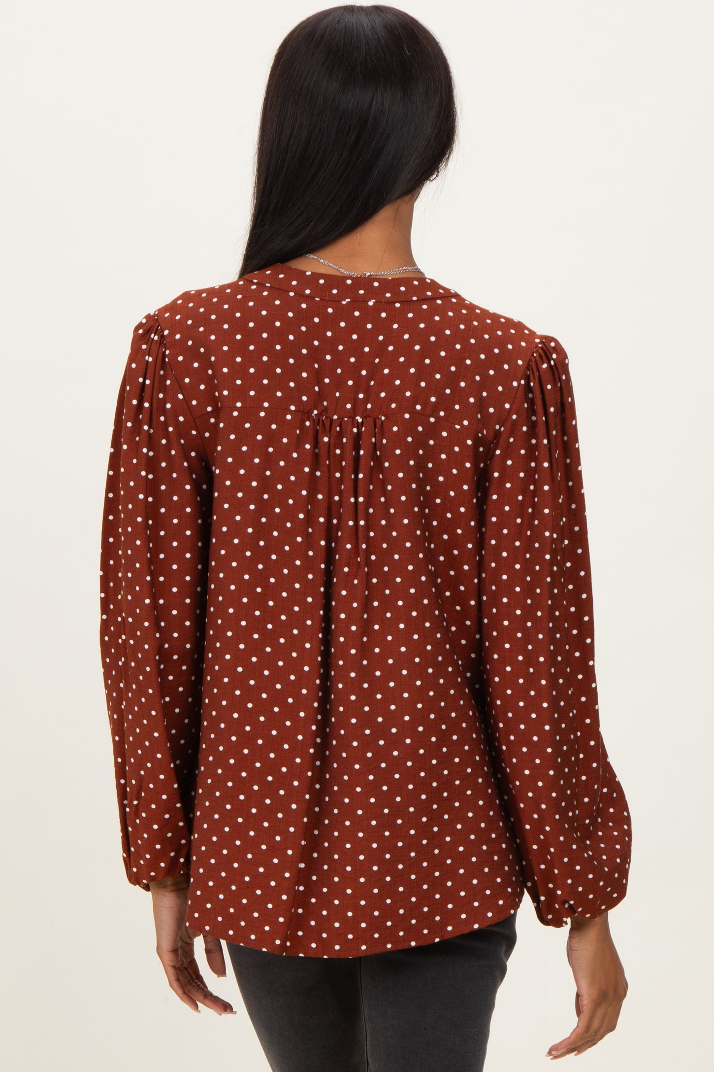 woman wearing a brown polka dot blouse with puff sleeves and a gathered back detail