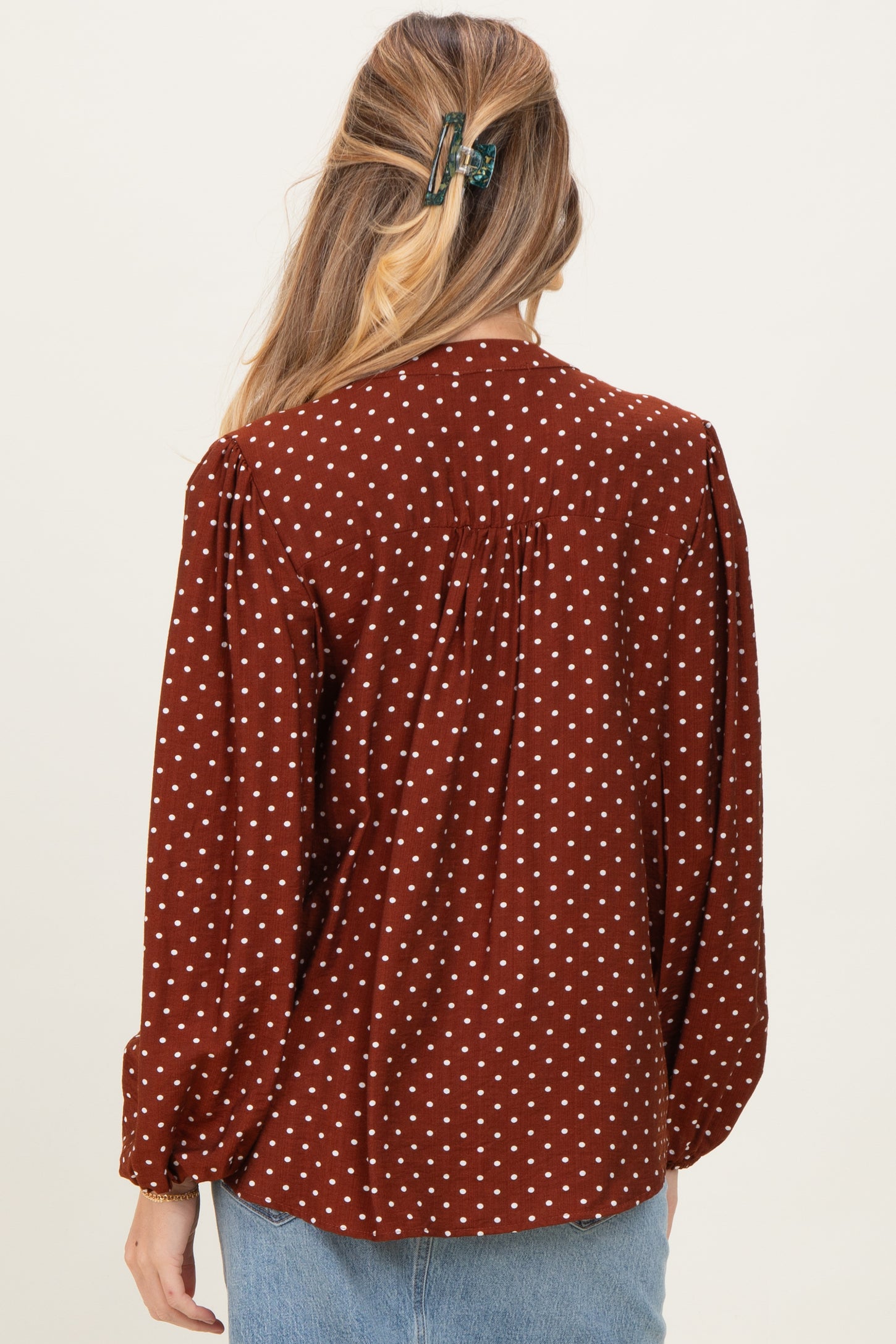 woman wearing a brown polka dot maternity blouse with a relaxed fit and back pleat detail