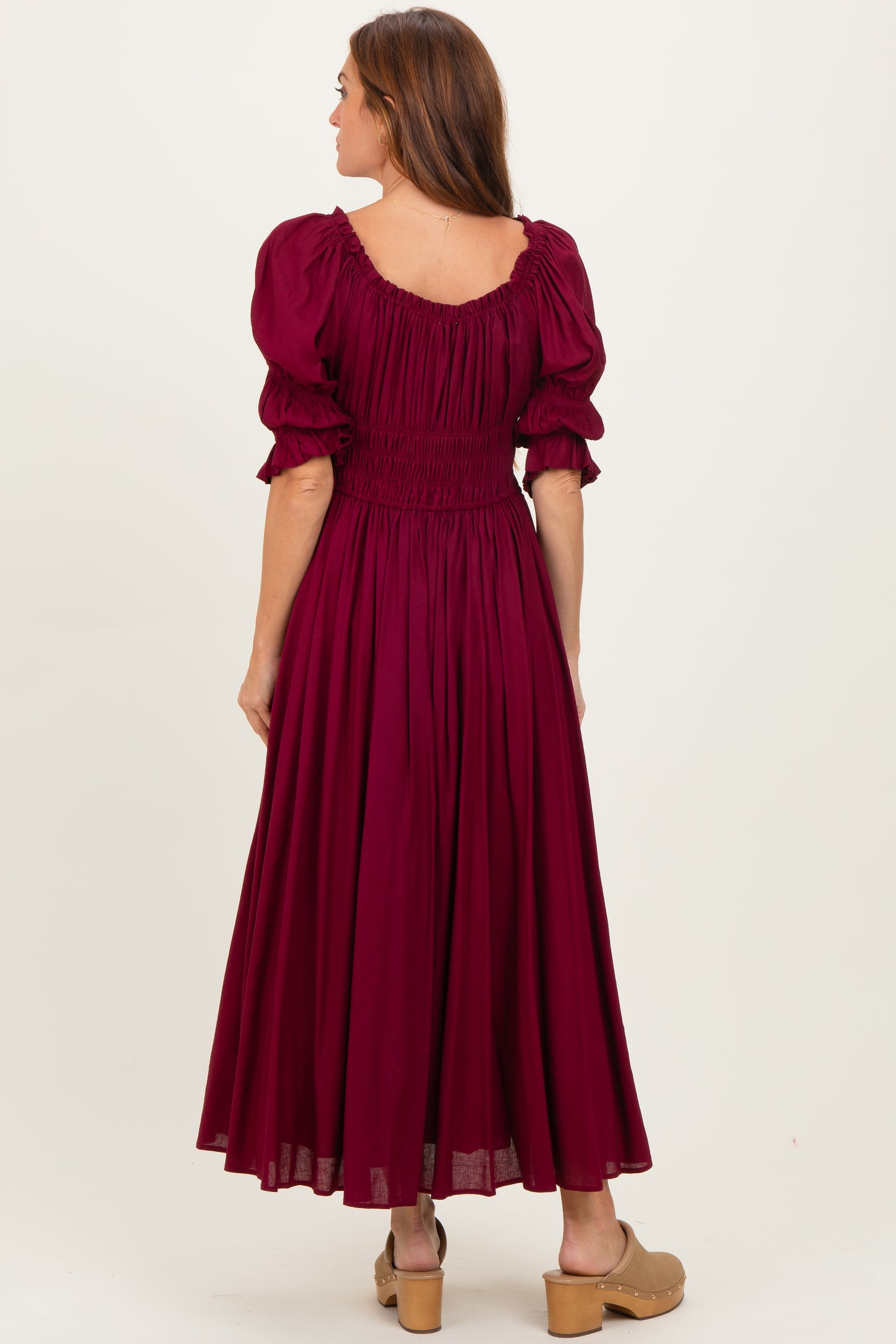 woman wearing a burgundy puff sleeve maxi dress with a smocked bodice and flowing skirt, viewed from the back