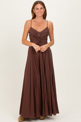 woman wearing a brown maxi dress with spaghetti straps and a cinched bodice, standing with hands clasped in front