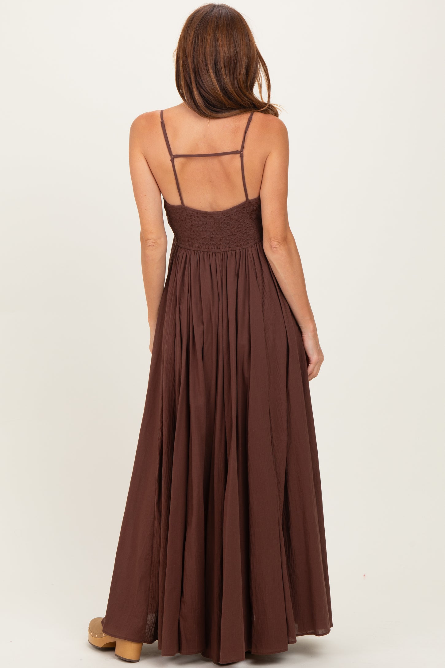 woman wearing a brown maxi dress with a smocked bodice and thin spaghetti straps, viewed from the back