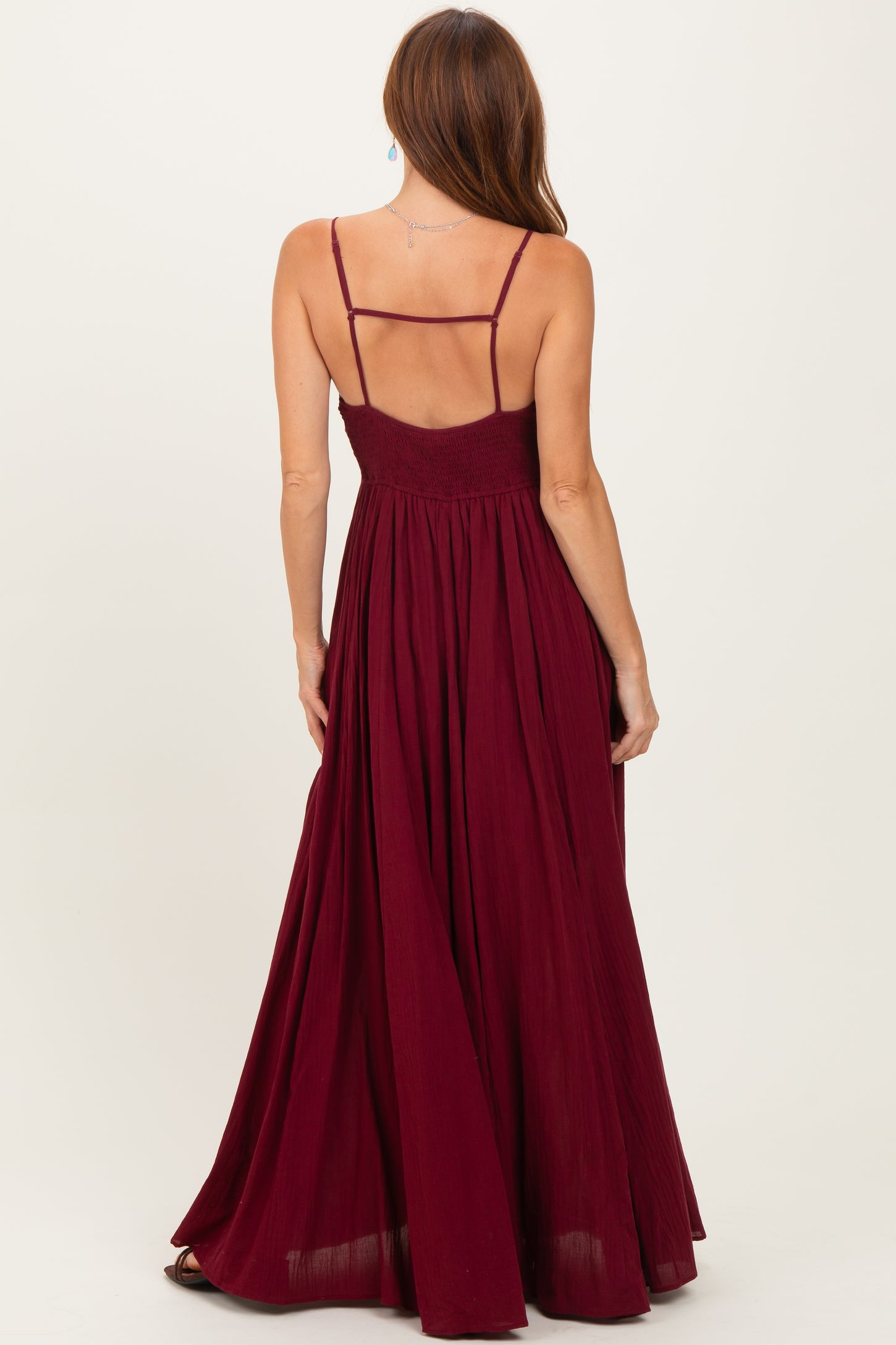 woman wearing a burgundy maxidress with spaghetti straps and a smocked back, shown from the back