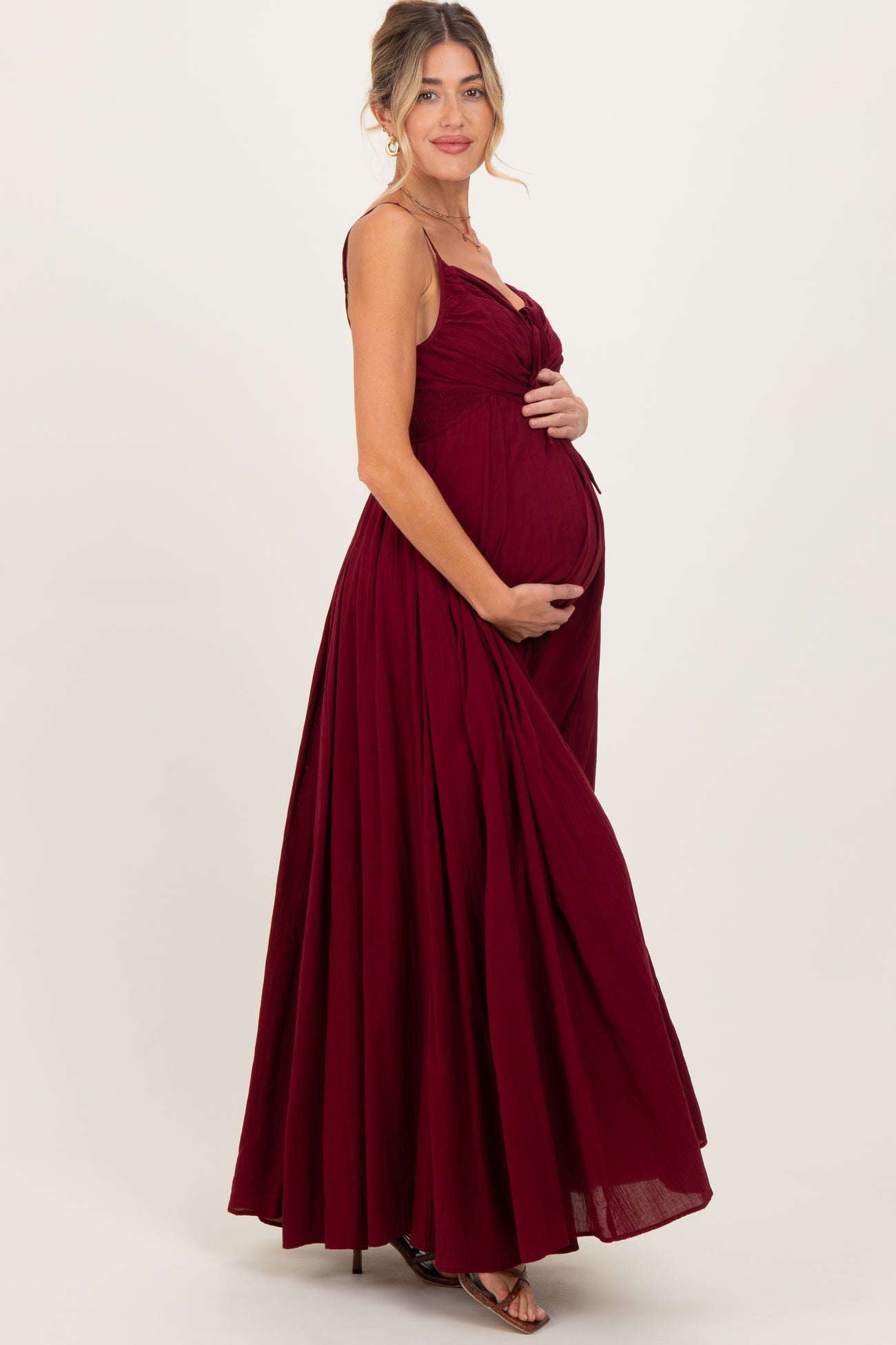woman wearing a burgundy maternity gown with a fitted bodice and flowing skirt, holding her baby bump