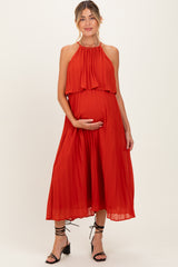 woman wearing a red pleated maternity dress with a halter neckline and holding her baby bump