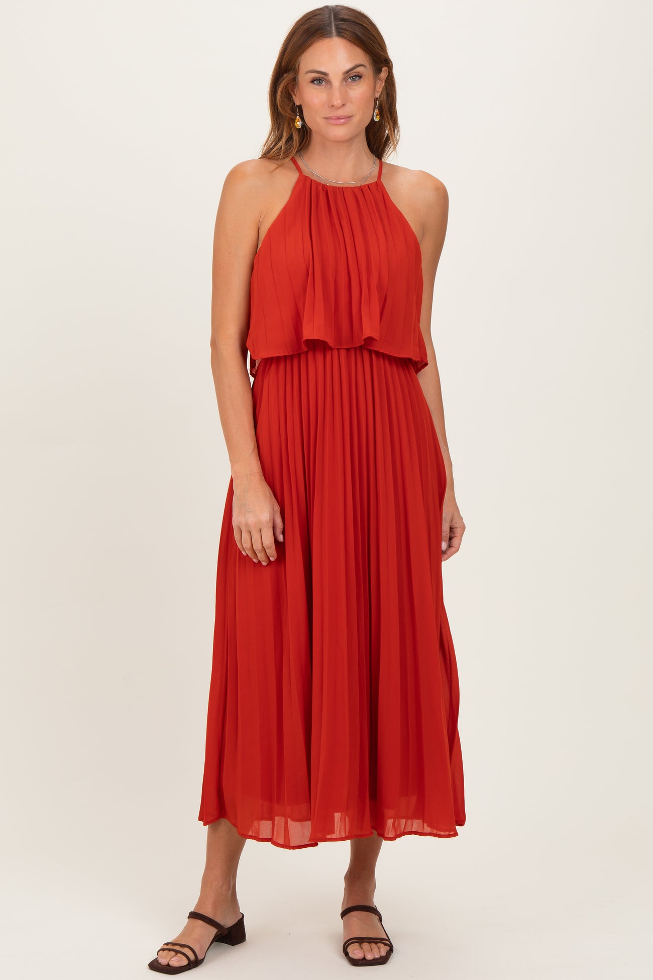 woman wearing a red sleeveless pleated maxi dress with a layered bodice and standing in a relaxed pose