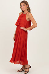 woman wearing a long red pleated dress with a halter neck and layered bodice, styled with strappy sandals