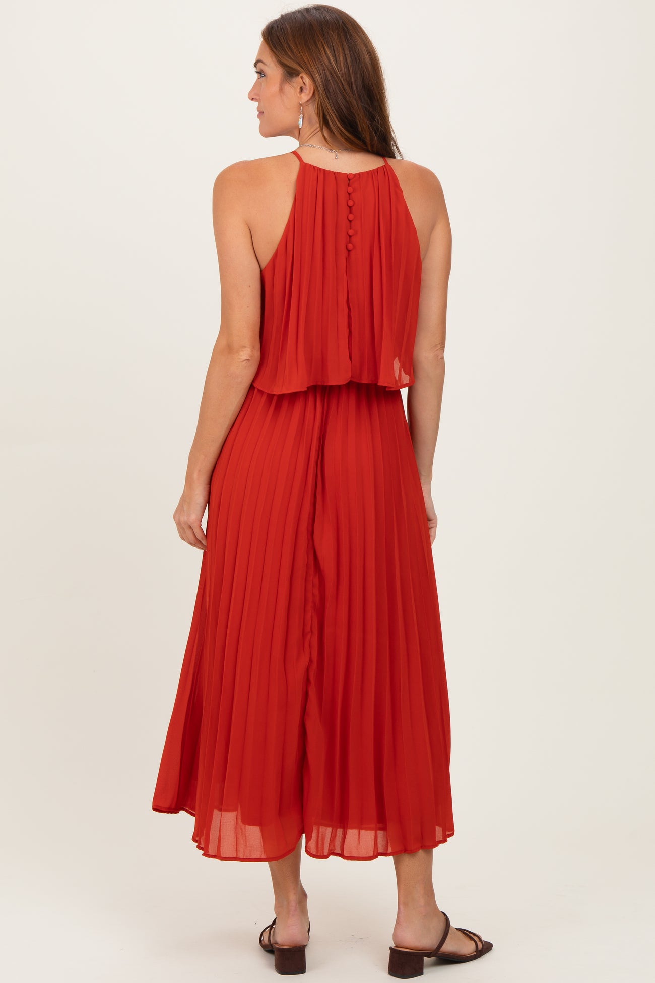 woman wearing a red pleated midi dress with a halter neck and button details on the back