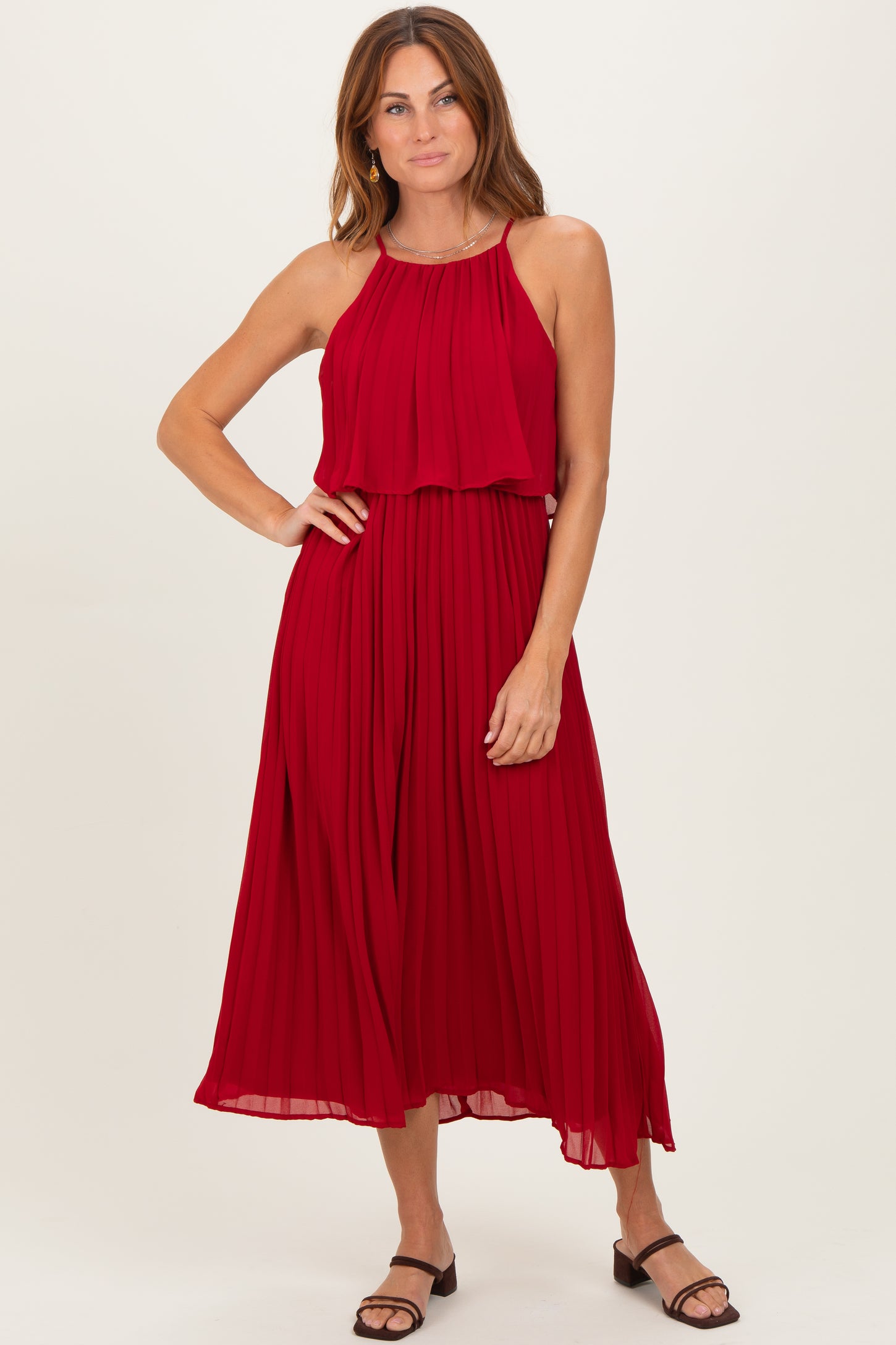 woman wearing a red pleated midi dress with a halter neckline and flowy skirt, styled with black sandals