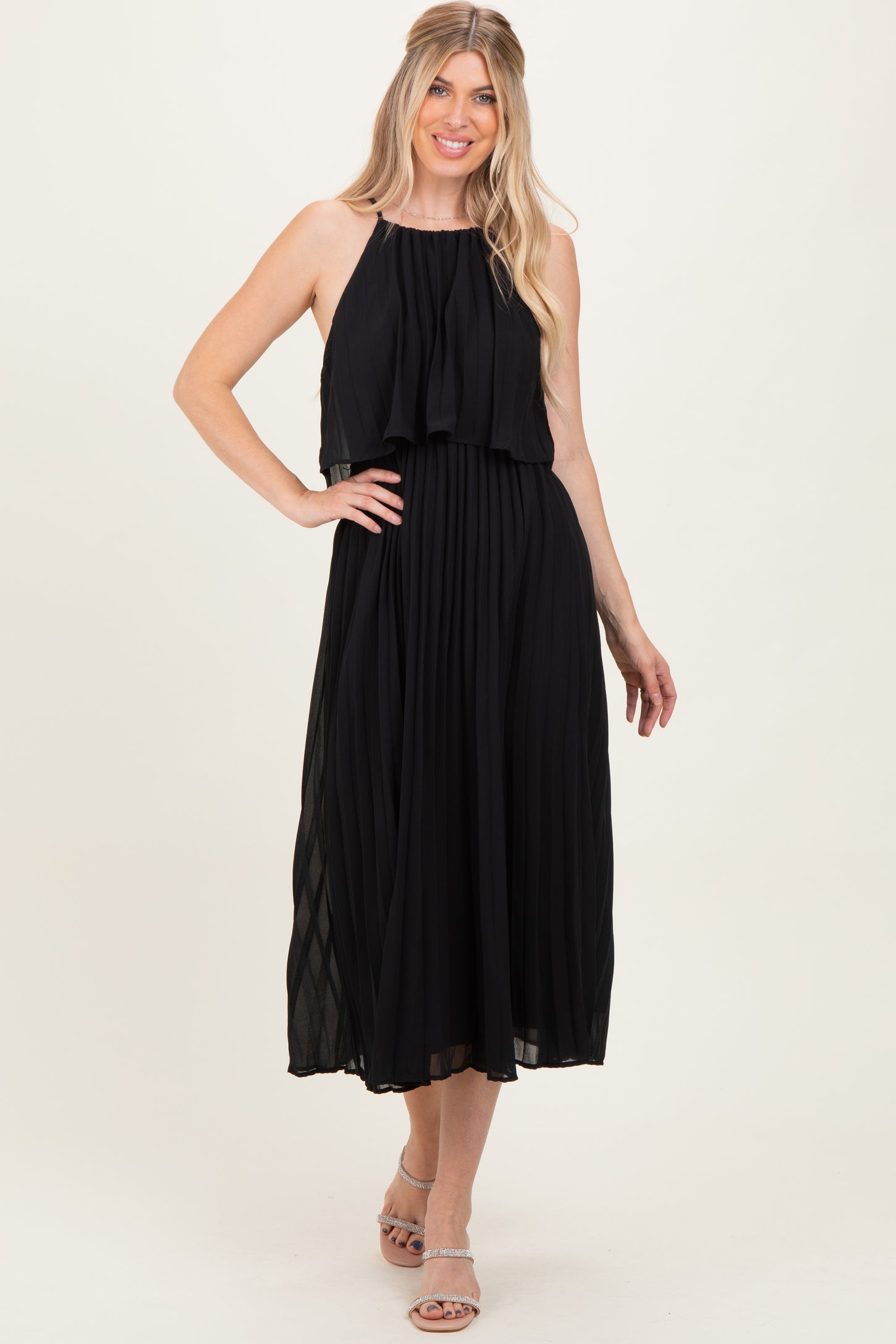 woman wearing a black pleated halter neck midi dress with a layered bodice and sandals