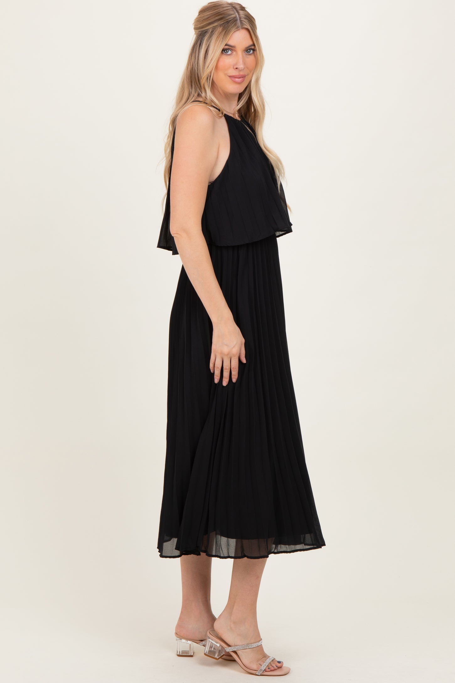 woman wearing a black pleated midi dress with layered top and a flowy silhouette, standing sideways