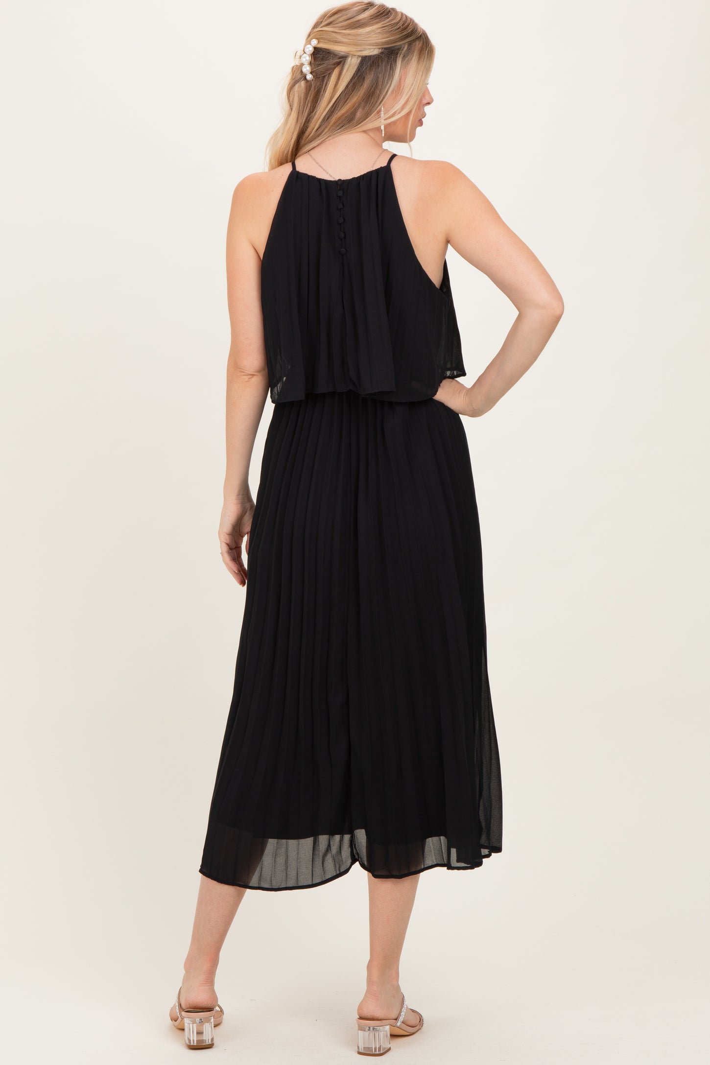 woman wearing a black pleated maxi dress with a flowing overlay and adjustable straps, viewed from the back