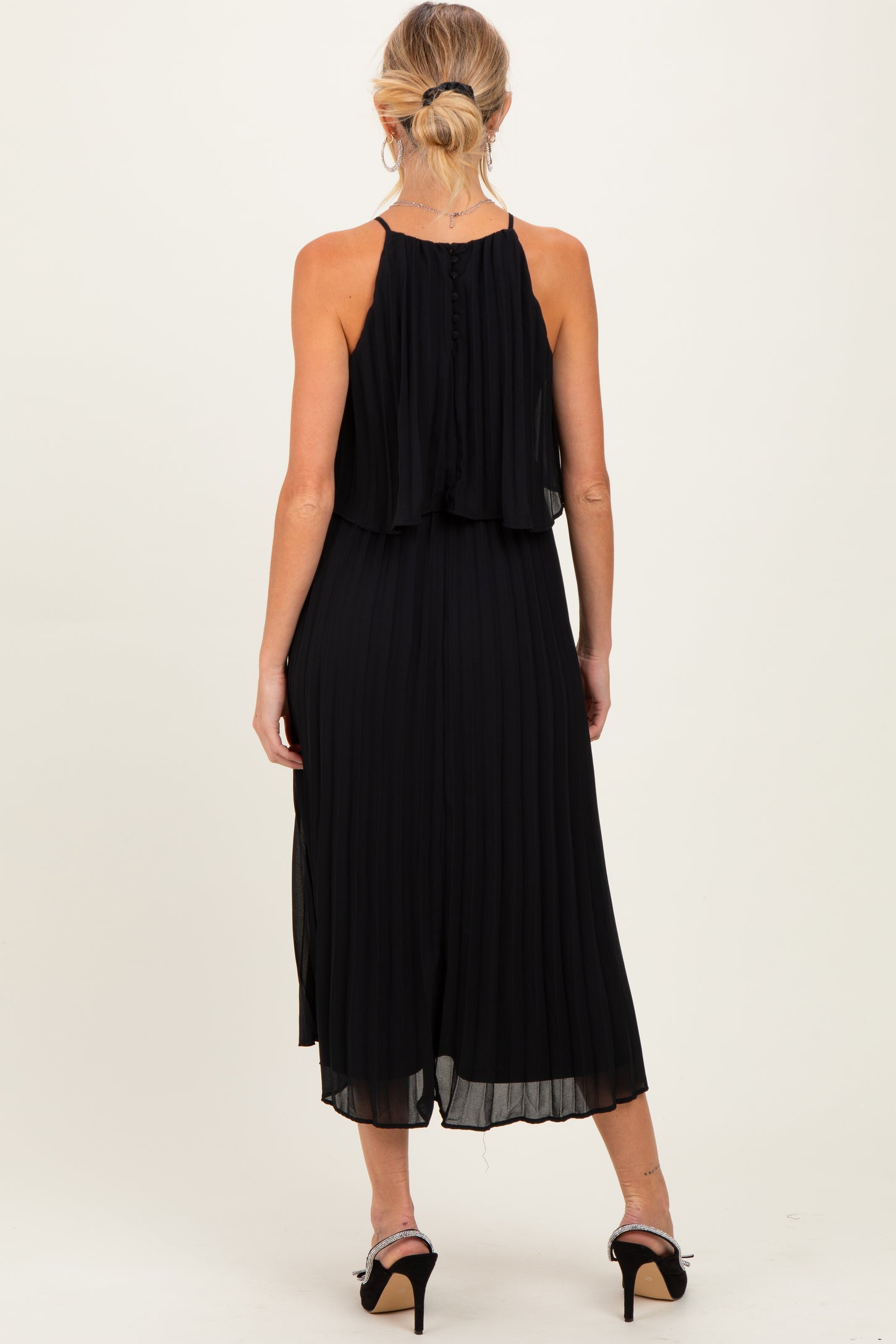 woman wearing a sleeveless black maternity dress with a pleated design and an open back, showcasing her baby bump