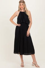 woman wearing a black pleated maxi dress with a halter neck and layered top, standing with one hand on her hip