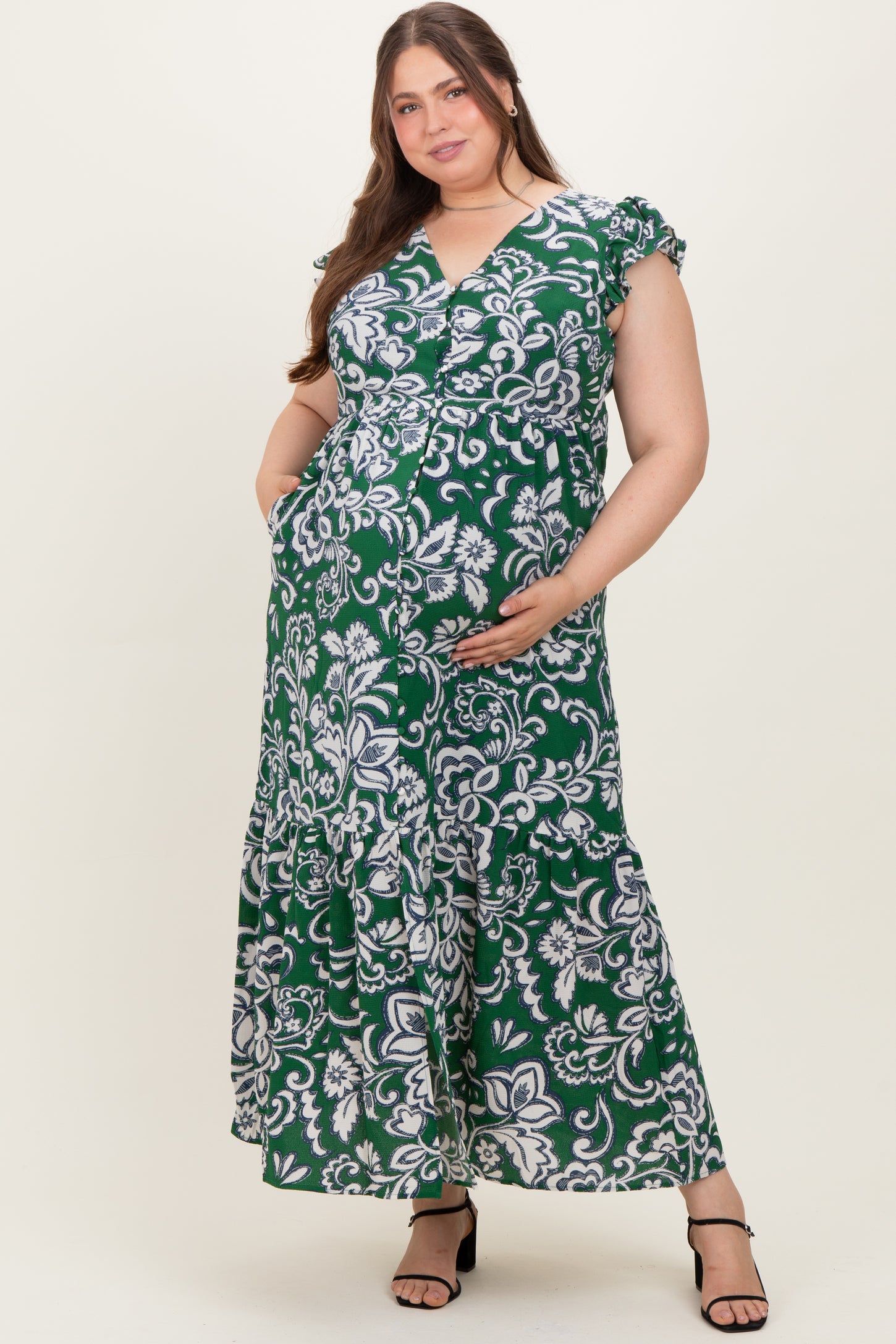 woman wearing a green floral maternity plus maxi dress with ruffled sleeves and a baby bump