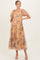 woman wearing a flowy yellow floral maternity dress with puff sleeves and a tiered skirt, holding her baby bump
