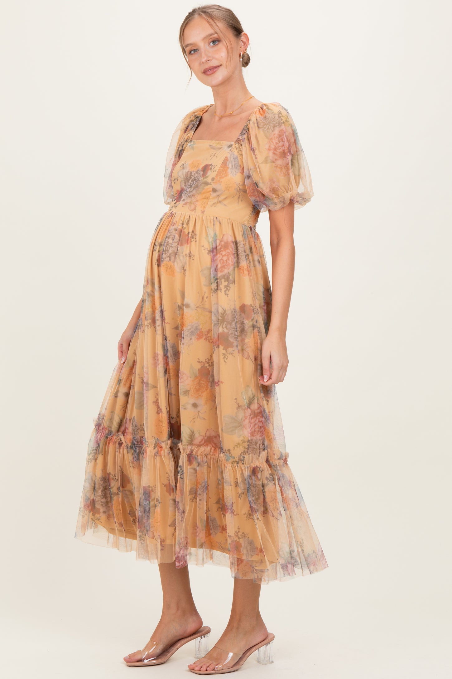 woman wearing a floral print maternity dress in soft yellow with puff sleeves and a tiered skirt, showcasing her baby bump