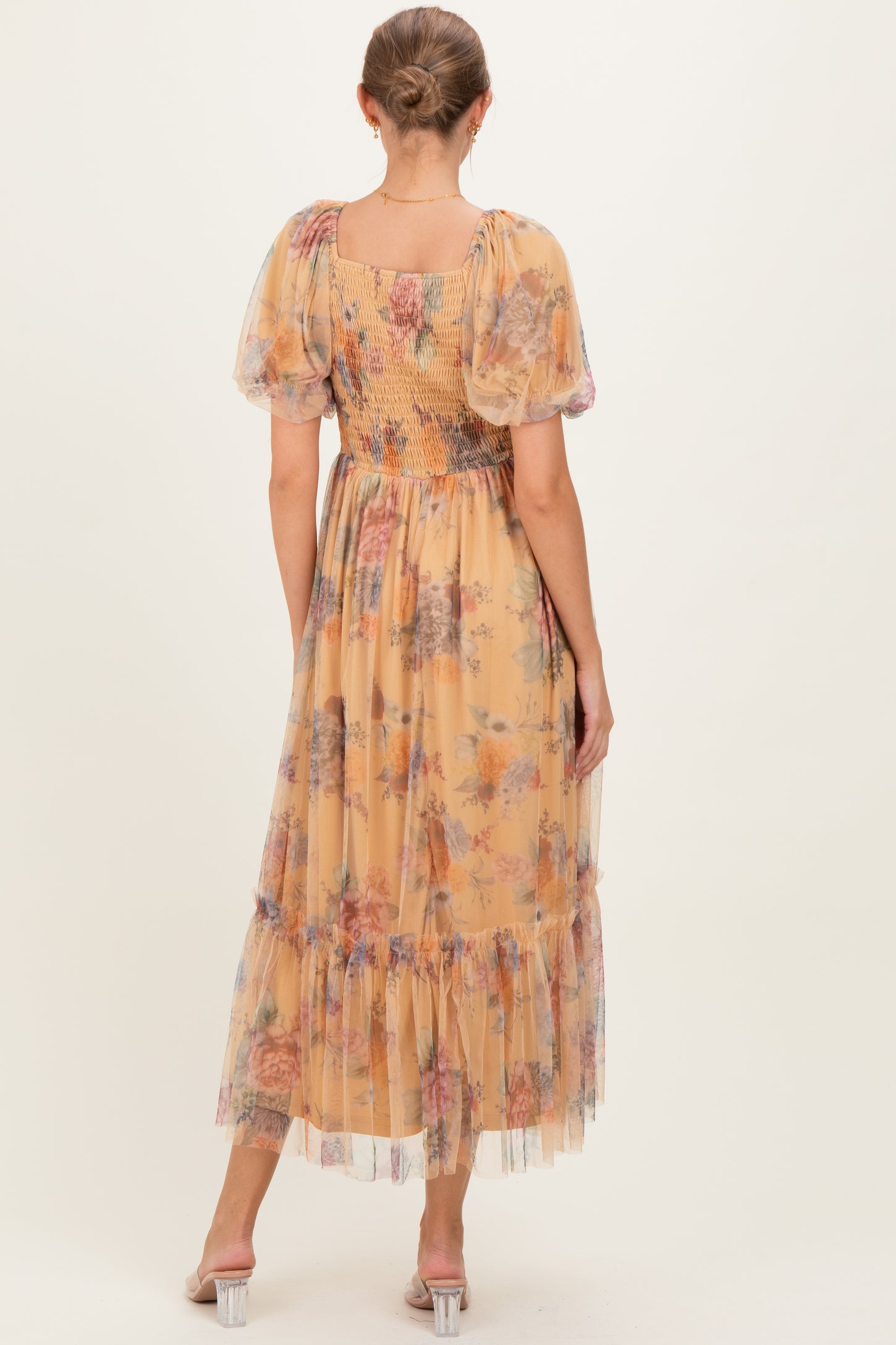 woman wearing a floral print maternity dress with puff sleeves and a back smocked detail, standing on a neutral background