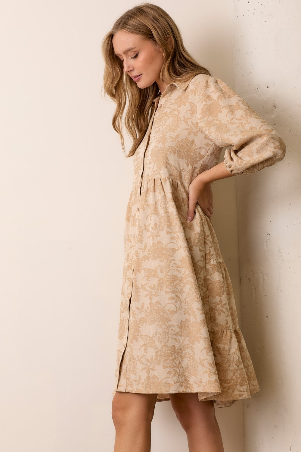 woman wearing a beige floral print button-up shirt dress with long sleeves and a tiered skirt