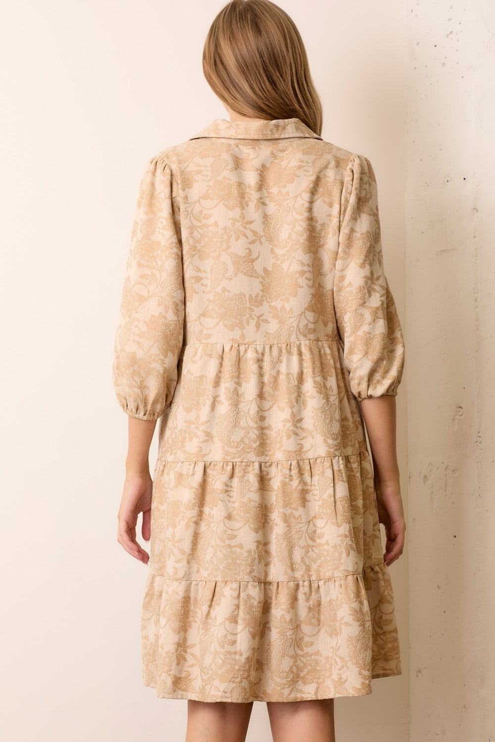 woman wearing a beige floral printed tiered dress with long puff sleeves and a collar, shown from the back
