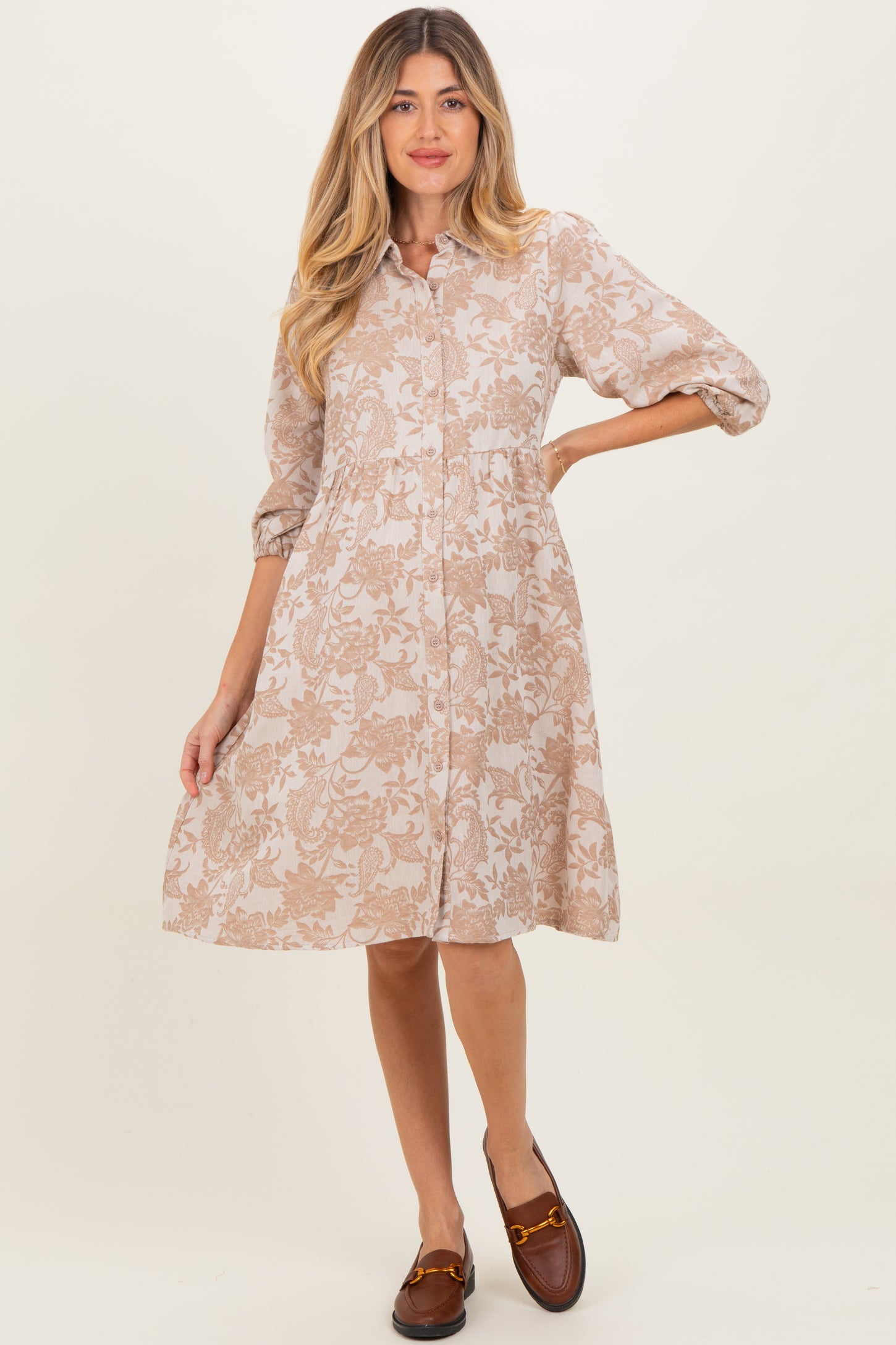 woman wearing a beige floral print maternity dress with a button-down front and three-quarter sleeves