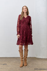 woman wearing a burgundy long sleeve lace dress with a smocked bodice and ruffled hem, paired with tan suede boots