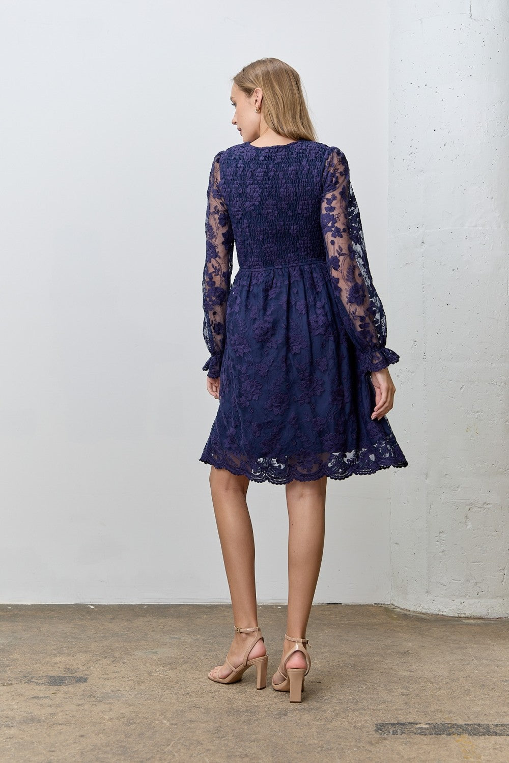woman wearing a navy blue lace dress with long sleeves and a flared skirt, shown from the back