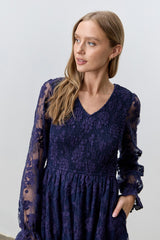 woman wearing a navy blue lace dress with long sleeves and a v-neckline, featuring floral details and a flowy skirt
