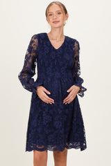 woman wearing a navy blue lace maternity dress with smocked bodice and long sleeves, holding her baby bump