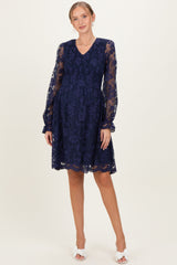 woman wearing a navy blue maternity lace dress with sheer long sleeves and a flowy skirt, showcasing a baby bump