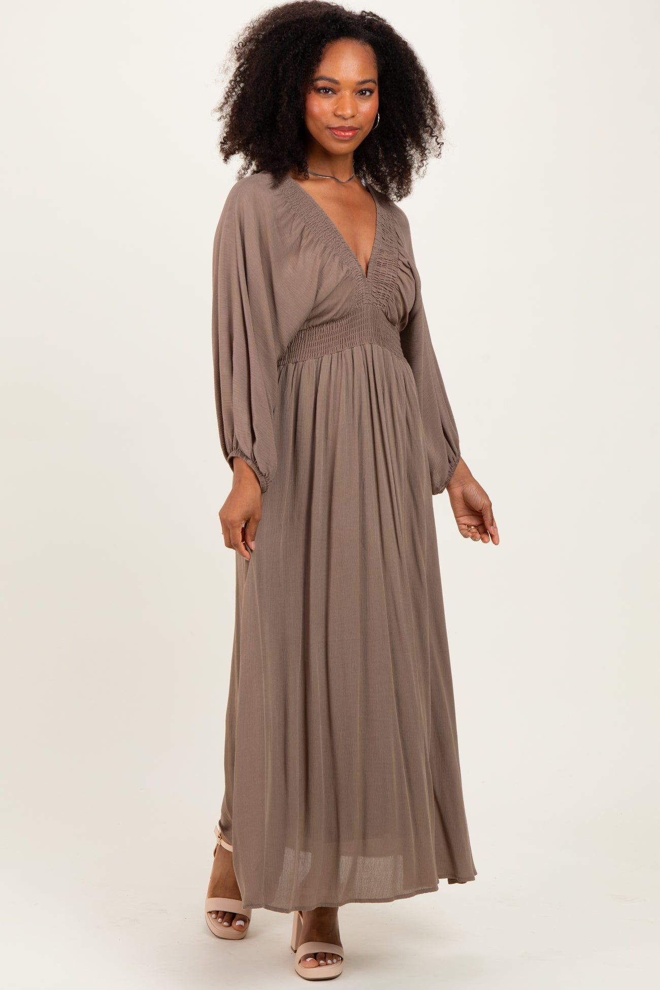 woman wearing a taupe long sleeve maxi dress with a smocked bodice and a flowing skirt