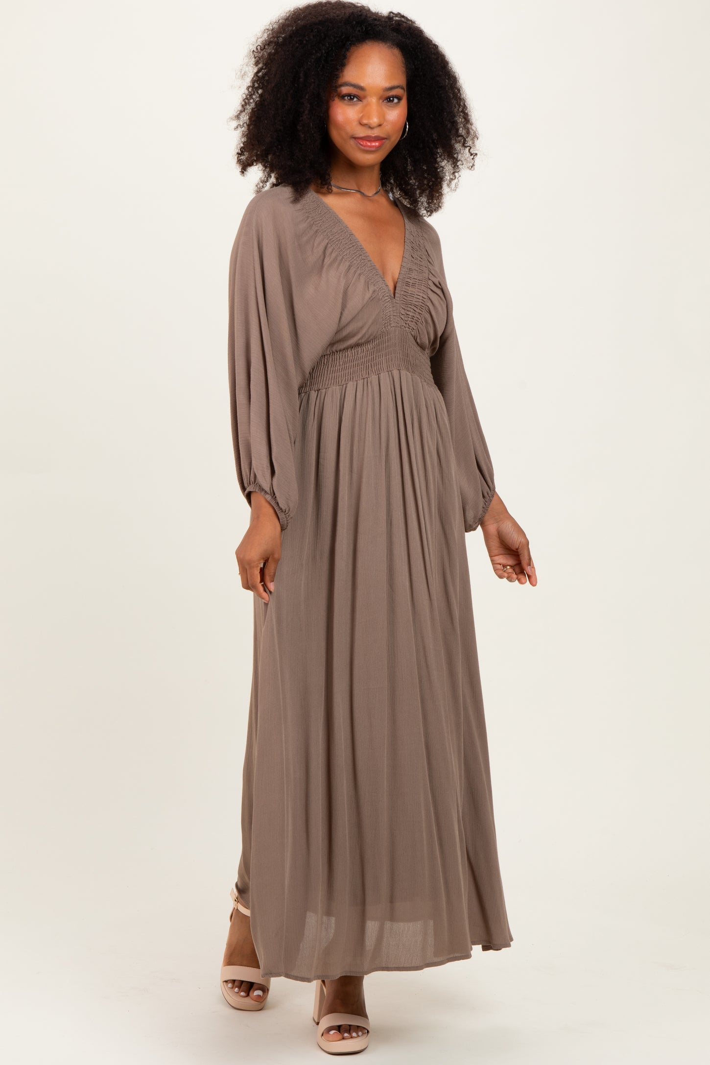 woman wearing a taupe long sleeve maxi dress with a smocked bodice and a flowing skirt