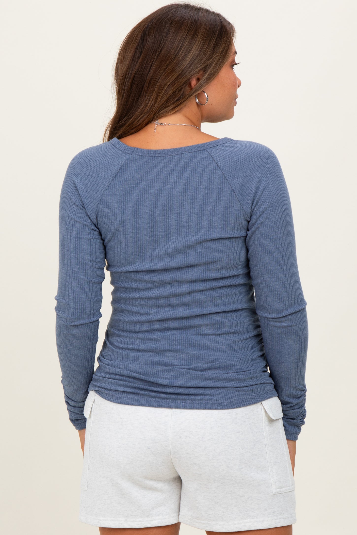 woman wearing a blue long sleeve maternity top, viewed from the back, paired with light gray shorts