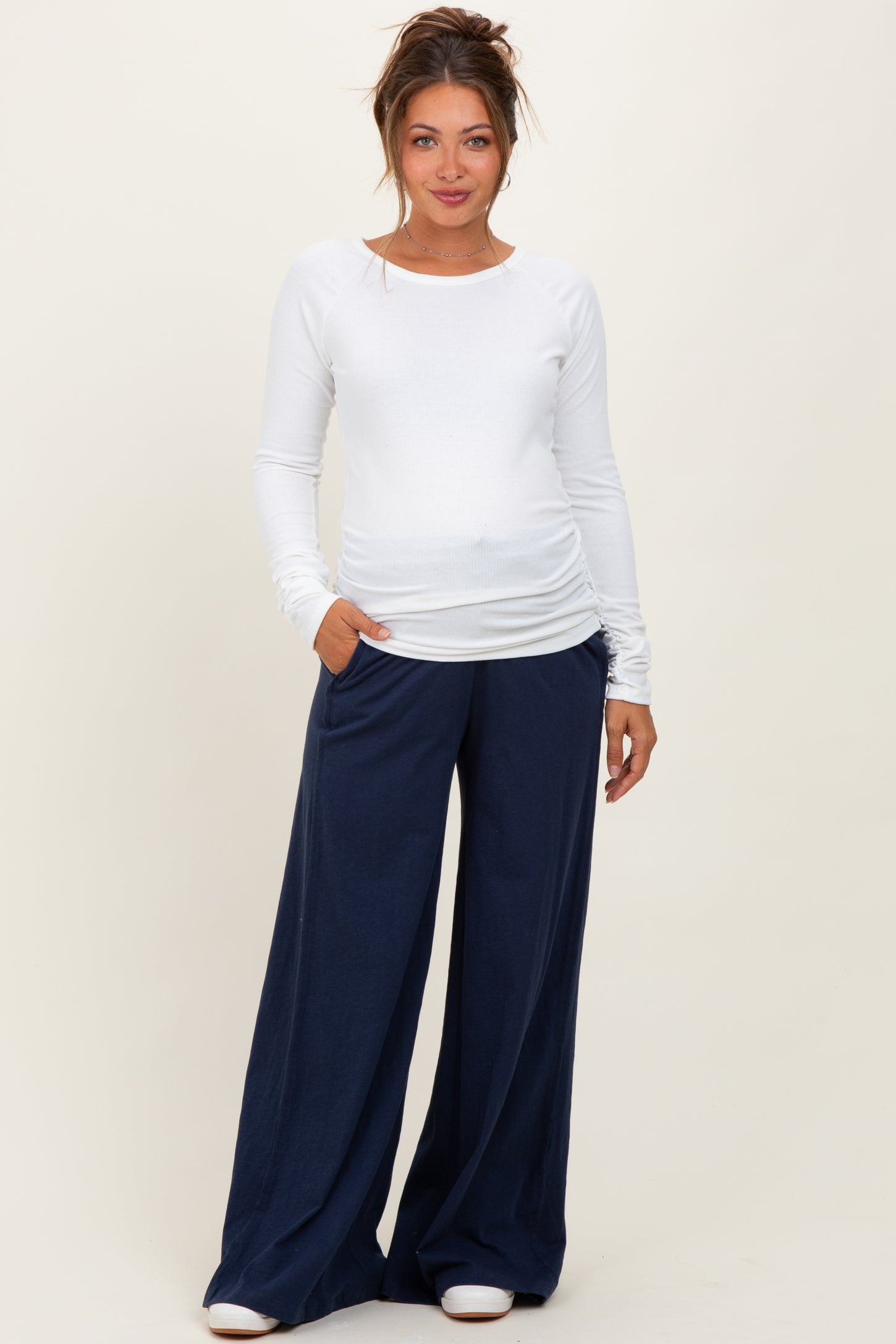 woman wearing a white long sleeve maternity top and navy wide-leg maternity pants, showing her baby bump