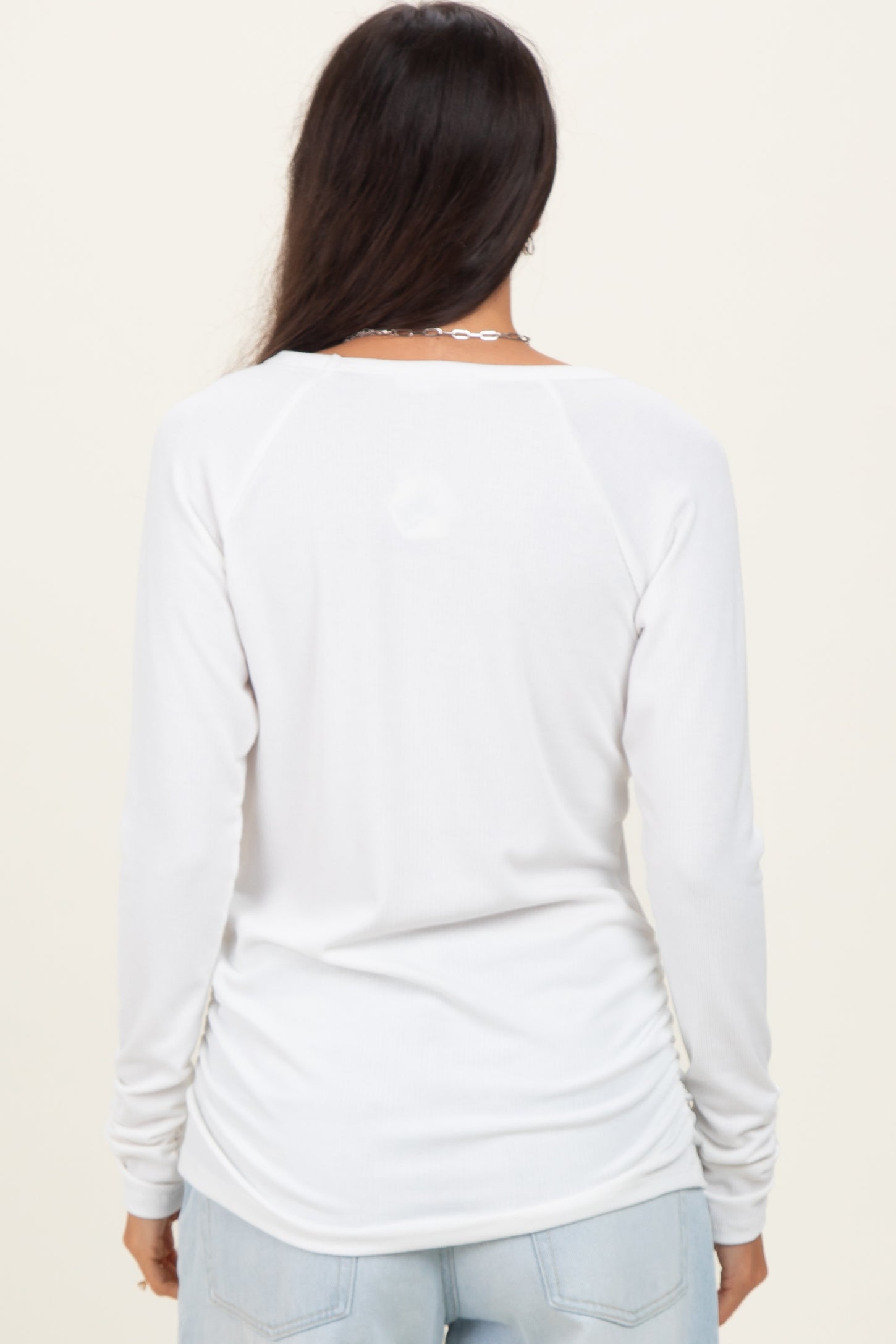 woman wearing a white long sleeve shirt with a curved hem and relaxed fit, viewed from the back