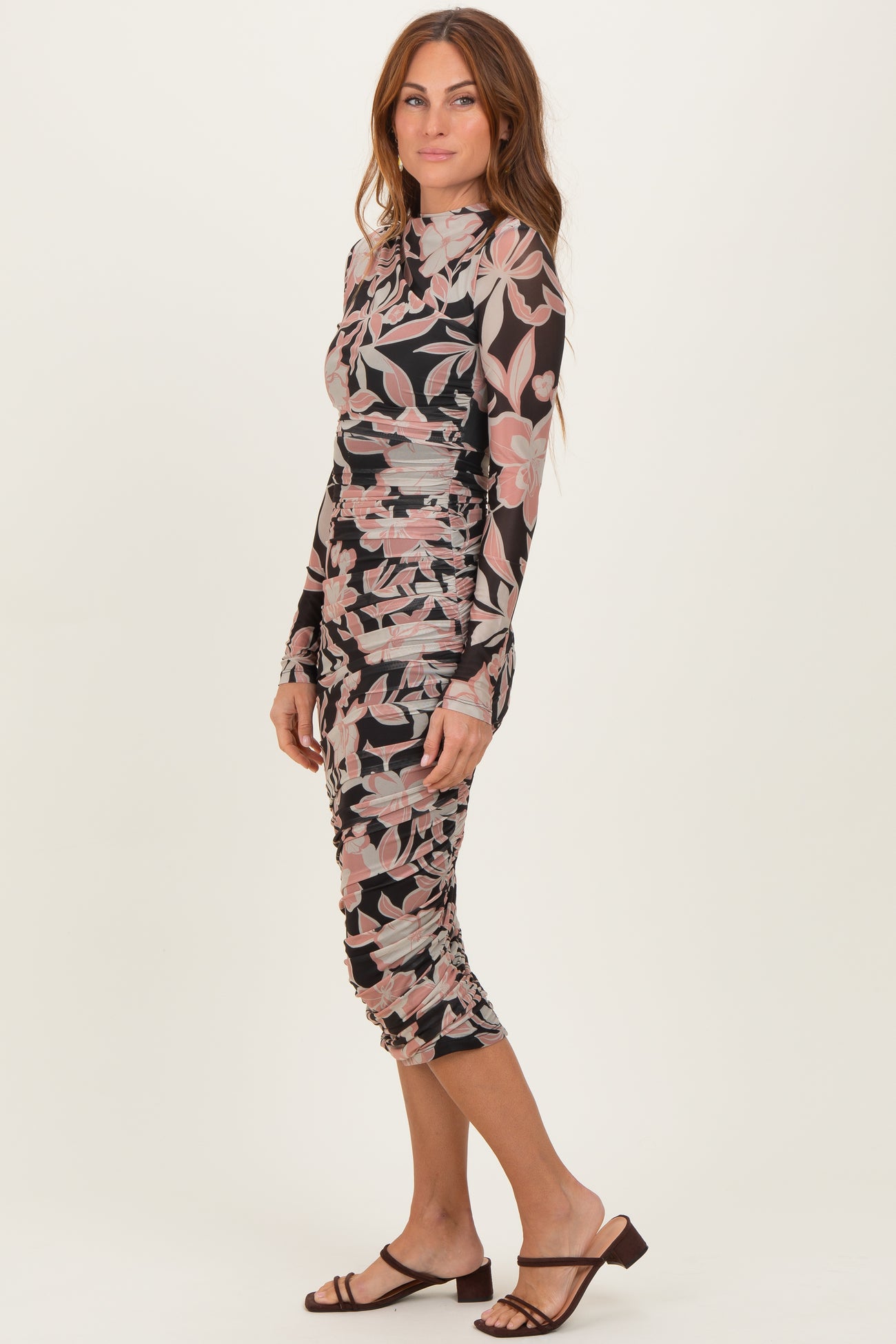 woman wearing a long sleeve floral print bodycon dress with ruched details and a mock neck, posed sideways