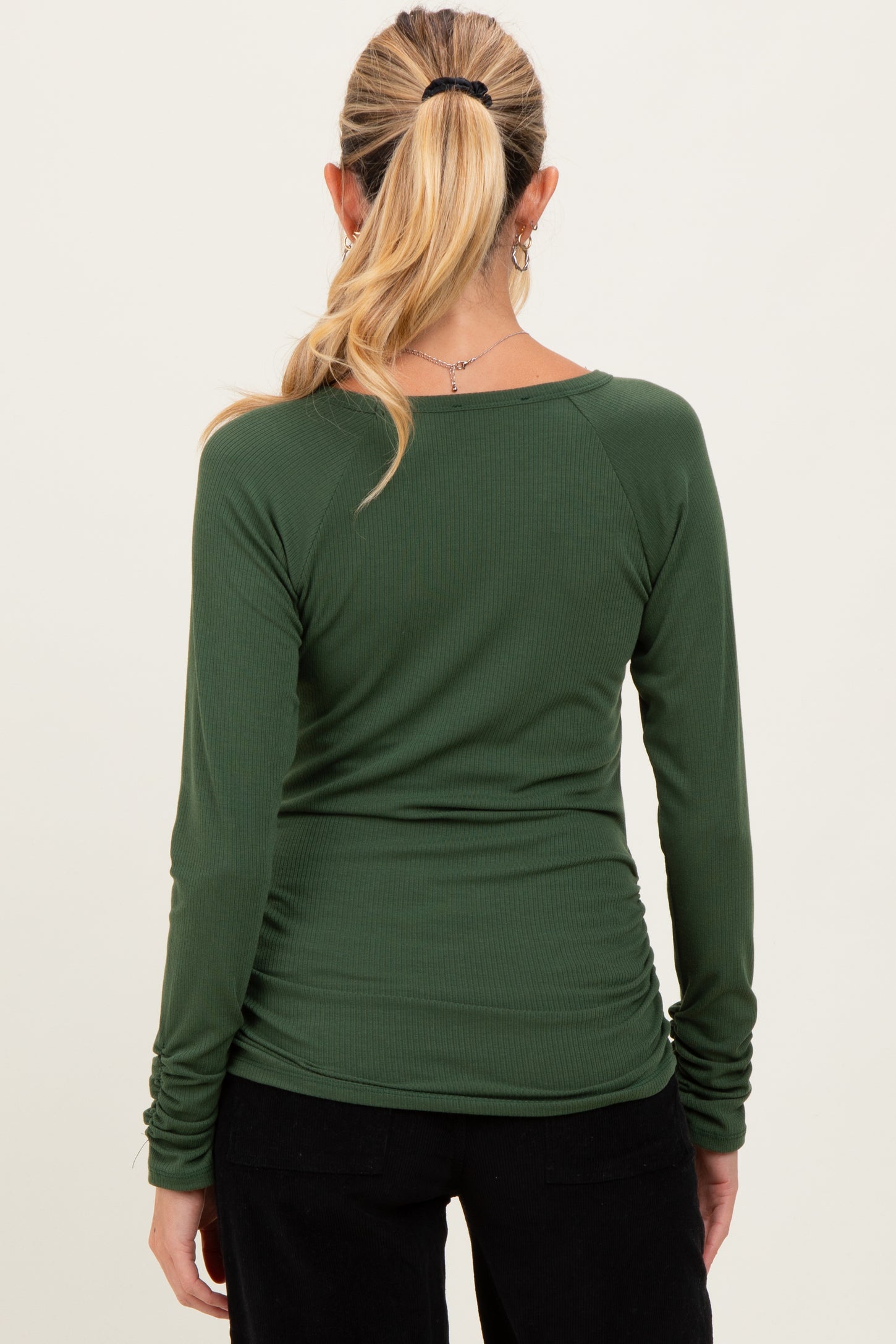 woman wearing a dark green long sleeve maternity top with ruching details at the sides
